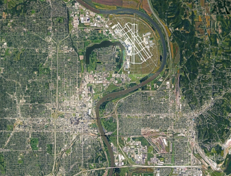 An aerial satellite view of a city with roads, buildings, and a river running through it.