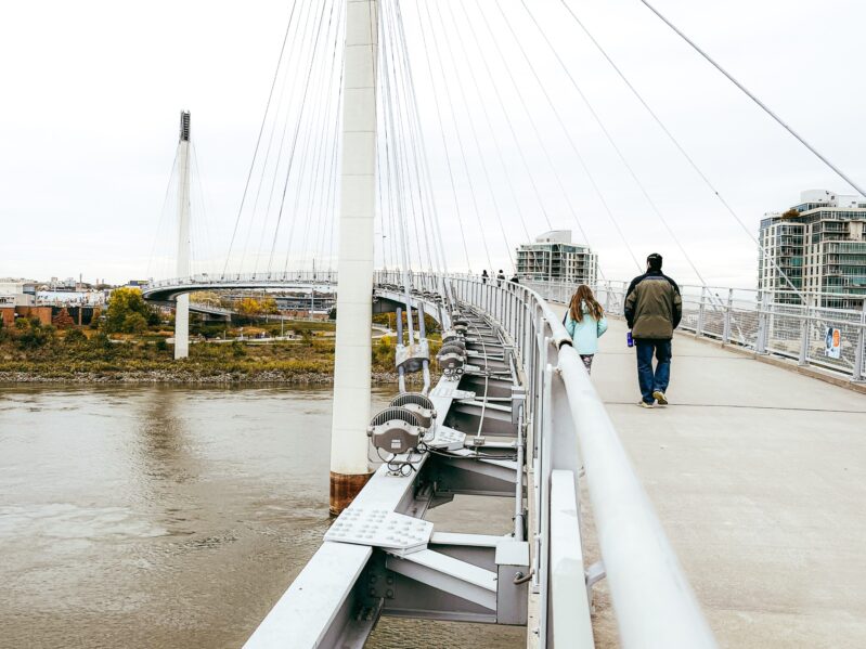 People walk across a modern pedestrian bridge with cables and railings.