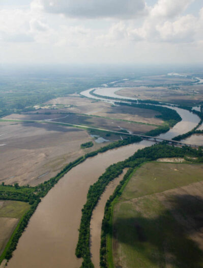 Wide muddy river winding through agricultural land and tree-lined banks.